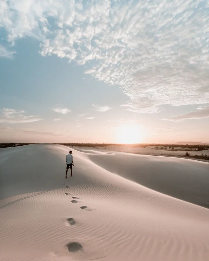 Einzelner Mann geht bei Sonnenuntergang über eine Sanddüne, Fußspuren im Sand