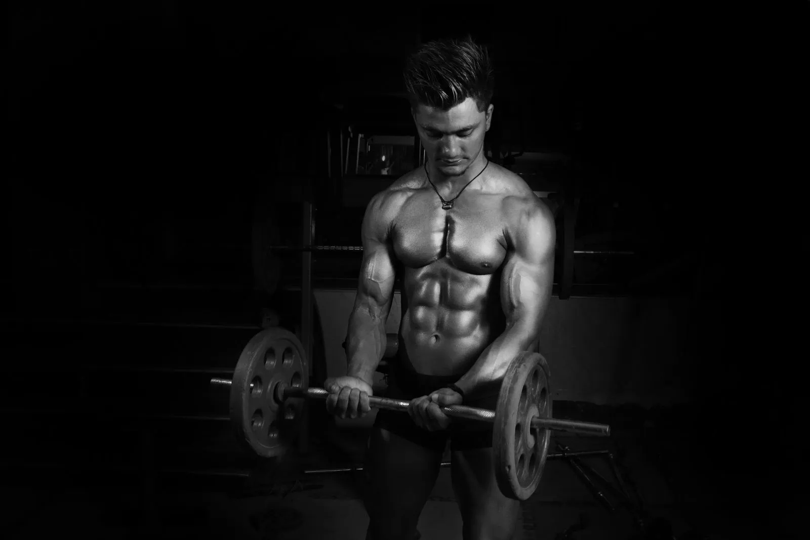 Schwarz-Weiß-Foto: Mann mit nacktem Oberkörper hebt im dunklen Gym eine Langhantel